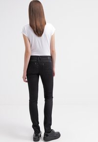 Černé slim-fit džíny s prostředním pasem, zadními kapsami a jemnými švy, doplněné obyčejným bílým tričkem s krátkým rukávem.