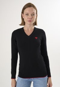 Schwarzer Pullover mit langen Ärmeln, V-Ausschnitt, roter Herzbestickung auf der Brust und kontrastierendem roten Saum an den Bündchen und am unteren Saum.