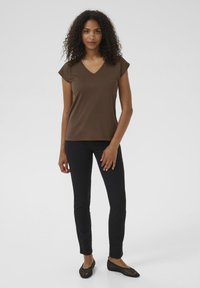 T-shirt marrone a V con maniche corte, abbinato a pantaloni neri slim-fit e ballerine nere in rete, caratterizzato da una texture liscia e un design semplice.