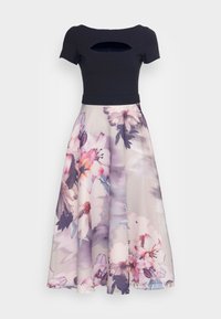 Top noir ajusté avec une ouverture en forme de clé, associé à une jupe plissée à imprimé floral dans des couleurs pastel de rose et de violet.