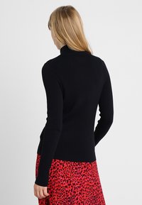 Pull en maille côtelée noir à col roulé, à manches longues, au design ajusté, associé à une jupe à imprimé léopard rouge et rose vibrant.