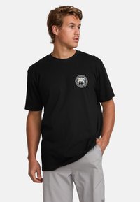 Black cotton t-shirt featuring a circular logo with a colorful mountain design on the left chest. Short sleeves and a relaxed fit.