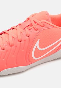 Nike lábbeli, élénk rózsaszín szintetikus felsőrésszel, hálós textúrával, kontrasztos fehér logóval és texturált szürke talppal.