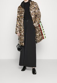 Abrigo de plumas con estampado de leopardo, capucha negra y cierre de cremallera; combinado con pantalones negros de pierna ancha y un pequeño bolso negro.