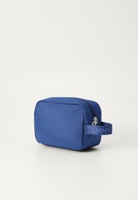 Borsa da toilette in tessuto blu con chiusura a zip, dotata di manico laterale e logo "TOMMY" in rilievo. Forma rettangolare e superficie testurizzata.