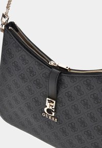 Sort Guess håndtaske med gentaget logo mønster, guld lynlås og guld kæderem, der har en fremtrædende guld "G" brand charm.