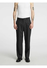 Svart plissert bukse med knappet midje, sidelommer og rett ben, laget av et glatt stoff. Brukes med svarte sko.