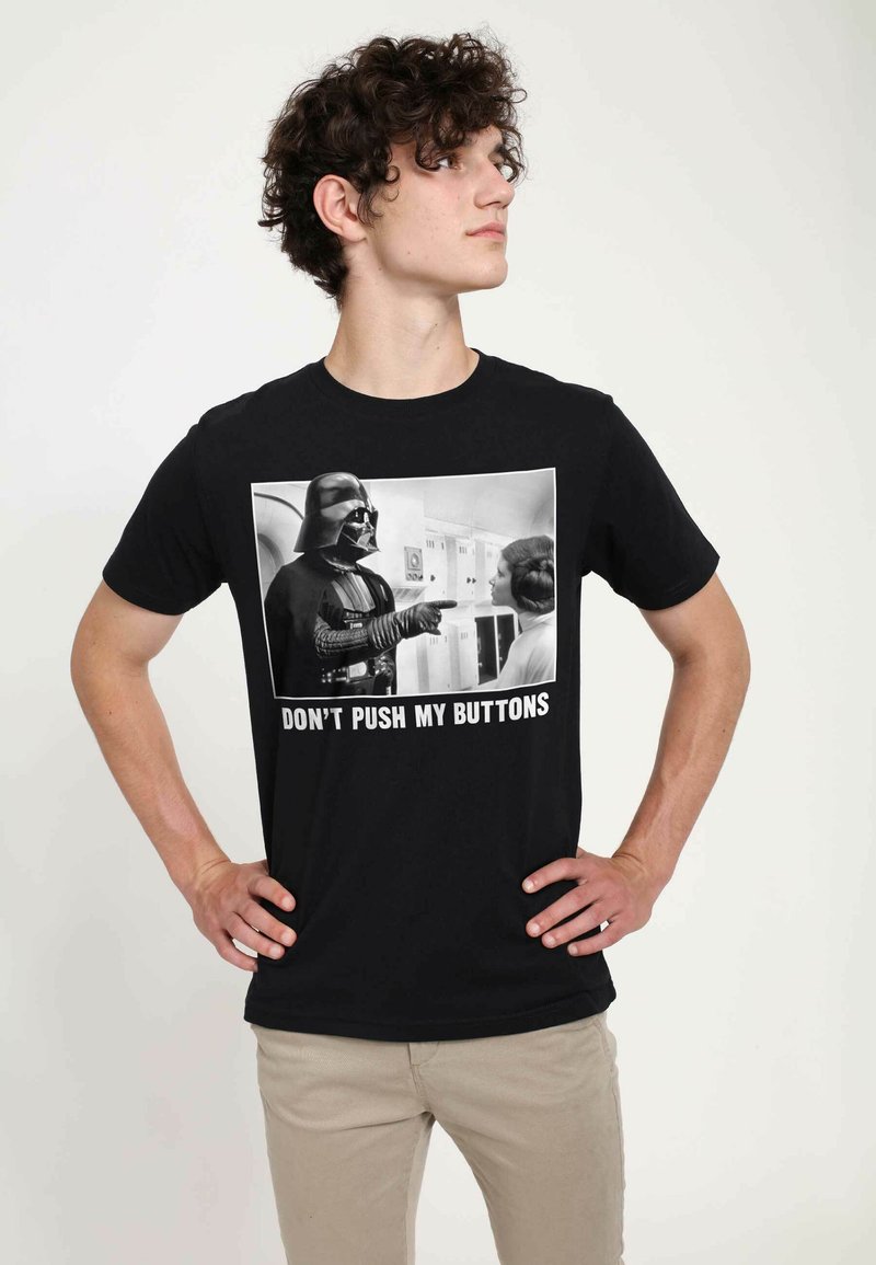 Černé bavlněné tričko s potiskem černobílého grafického zobrazení interakce postav, s textem "NEPŘIDÁVEJ MI NA STAROSTECH" pod tím.