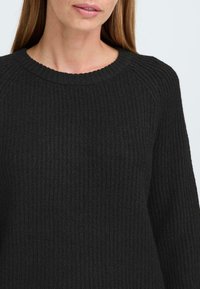 Pull en maille côtelée noire avec un col rond et des manches longues, mettant en valeur un tissu texturé pour chaleur et confort.