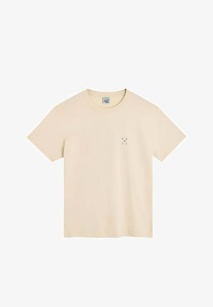 T-shirt beige à manches courtes et col rond avec un petit texte noir disposé verticalement sur le côté gauche de la poitrine indiquant "POULLIN".
