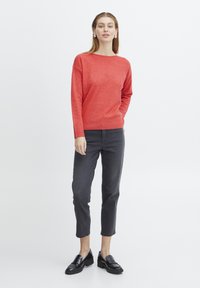 Pull en tricot rouge à manches longues et décolleté bateau, associé à un jean court gris et des mocassins noirs. Texture lisse, coupe décontractée.