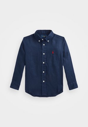 Camisa azul marino de manga larga con botones, cuello abotonado y logo bordado en rojo en el pecho izquierdo.