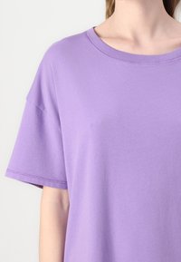 Violet trumpas rankovės marškinėliai, pagaminti iš minkštos medžiagos, su laisvu siluetu ir apvalia iškirpte, su subtiliomis siuvimo detalėmis ant krašto.