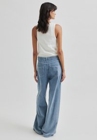 Világoskék, csíkos, bő szárú farmernadrág magas derékkal és két hátsó zsebbel, egy hozzá illő, testhez simuló, ujjatlan fehér toppal párosítva.