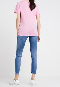 Rosa bomullströja med korta ärmar, tillsammans med ljusblå skinny jeans och vita sneakers, sedd bakifrån.