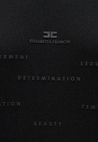 Μαύρο ύφασμα με ανάγλυφα γράμματα που περιλαμβάνουν λέξεις όπως "αποφασιστικότητα" και "ομορφιά", μαζί με το όνομα της μάρκας "Elisabetta Franchi" σε κομψό λογότυπο.