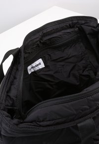 Sac en nylon noir avec compartiment principal zippé, poche intérieure et étiquette Converse. Texture lisse et sangles de poignée robustes.