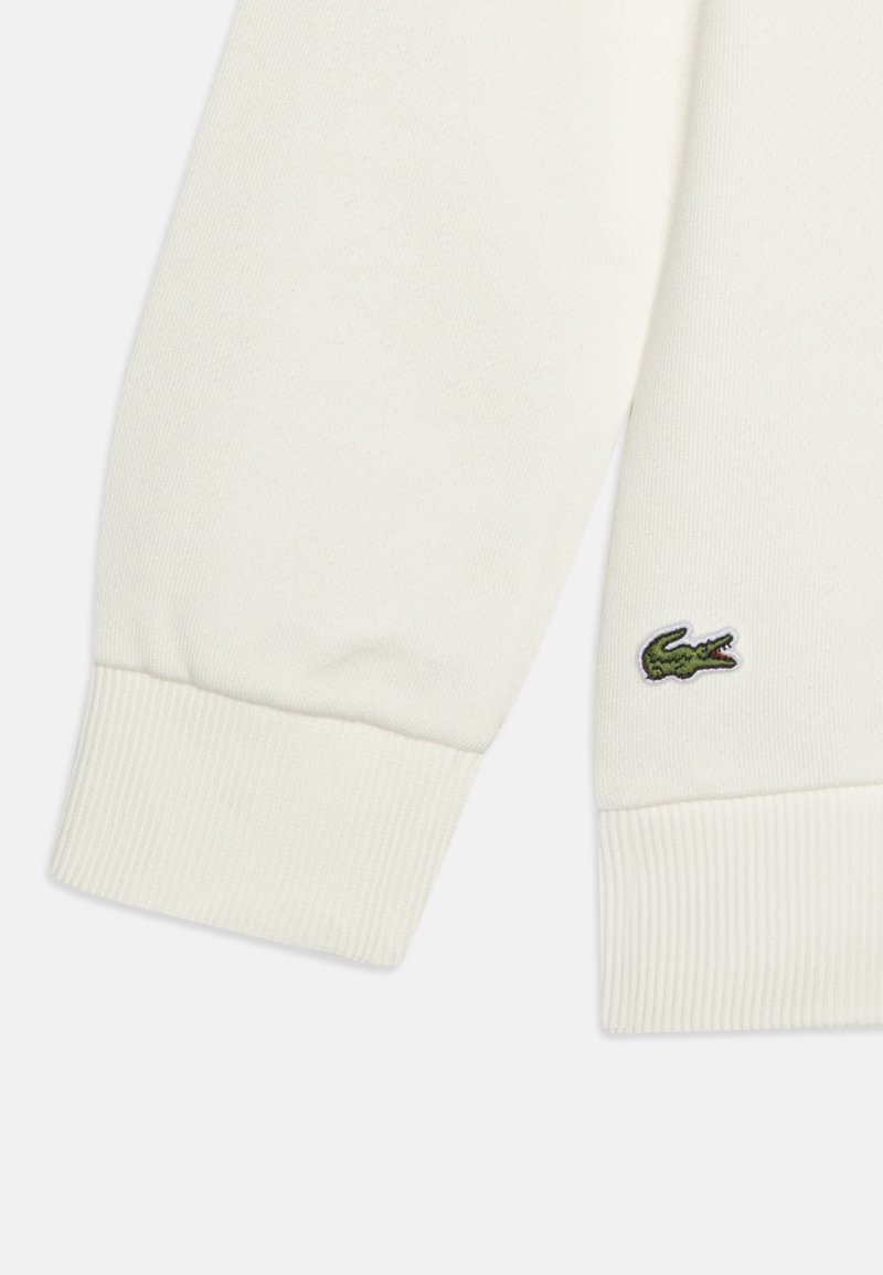 Manche de sweat-shirt blanc avec un poignet côtelé. Logo de crocodile vert brodé sur le haut de la manche. Tissu doux avec une texture lisse.