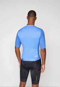 Modrý cyklistický dres s krátkým rukávem, úzkého střihu, se zadními kapsami, v kombinaci s černými šortkami s výstelkou a reflexními prvky.
