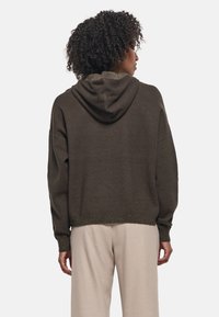 Sudadera con capucha marrón con un acabado texturizado y puños elásticos, combinada con pantalones ligeros de corte holgado. Ajuste casual y relajado.