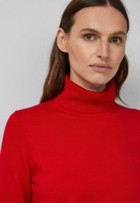 Czerwony sweter z golfem, wykonany na sposób dopasowany. Miękka tekstura i żebrowany kołnierz. Posiada długie rękawy i brak widocznych wzorów lub akcentów.