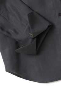 Chemise à manches longues gris foncé avec poignets boutonnés, soigneusement pliée sur un fond blanc, montrant la texture du tissu et les détails des coutures.