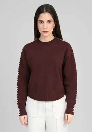 Pull en tricot bordeaux avec un col rond côtelé et des poignets. Présente des surpiqûres décoratives blanches le long des manches.