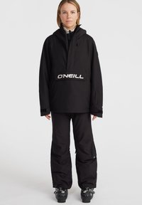 Čierna snehová bunda a nohavice majú voľný strih, zips, nastaviteľnú kapucňu a výrazné biele logo cez hruď.