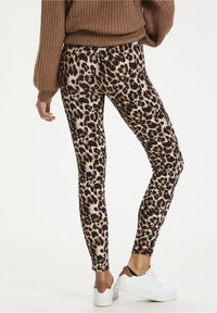 Leopardmönstrade leggings med en figurnära design, som har en blandning av ljusbruna och svarta fläckar på en beige bakgrund, parat med vita sneakers.