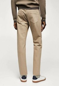 Beige Baumwollhosen mit geradem Schnitt, zwei Gesäßtaschen und einem strukturierten Bund, kombiniert mit weißen Sneakers mit schwarzem Akzent.