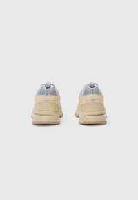 Vue arrière de baskets avec une tige en maille grise, des accents en caoutchouc beige, un talon texturé et une semelle beige. Détails réfléchissants à l'arrière.