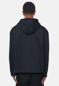 Schwarzer übergroßer Hoodie mit Kapuze und Zugband, weicher Textur, gerippten Bündchen und entspannter Passform, mit geradem Saum.