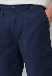 Marineblauwe linnenmix broek met een ontspannen pasvorm, voorzakken en een gladde textuur, met een enkele knoopsluiting in de taille.