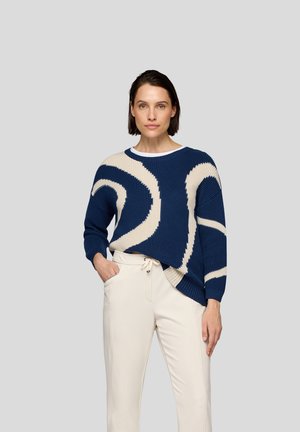 Blauer Strickpullover mit cremefarbenen, verschwommenen Mustern, runder Ausschnitt und gerippten Bündchen, kombiniert mit cremefarbenen Hose mit Kordelzug.