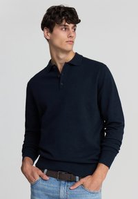 Polo a maniche lunghe blu navy con colletto, caratterizzato da dettagli con bottoni. Il tessuto appare liscio e a costine ai polsini.