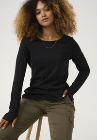 Schwarzes Langarmshirt mit Rundhalsausschnitt, weichem Stoff und Fingerlöchern, kombiniert mit olivgrünen, figurbetonten Hosen mit seitlichen Taschen.