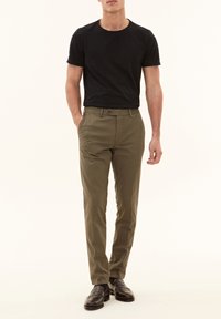 T-shirt nera a collo giro e chinos verde oliva. I chinos presentano tasche frontali e chiusura con bottone. Il modello indossa mocassini marrone scuro.