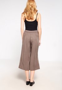 Bruine wijde broek met een gladde textuur en een elastische tailleband, gecombineerd met een zwart aansluitend tanktopje en zwart schoeisel.