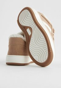 Chaussures en daim marron avec une semelle en caoutchouc blanche et une doublure en fausse fourrure, dotées d'une semelle extérieure texturée et d'un design minimaliste.