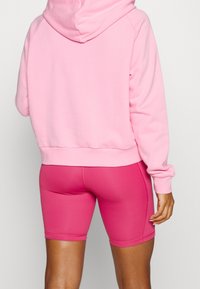 Hoodie rose avec capuche, en tissu doux, assorti à un short de vélo rose moulant. Texture lisse, sans motifs ni accents visibles.