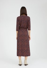 Robe marine avec un motif floral en rouille et orange, manches trois-quarts, taille cintrée et longueur cheville, associée à des bottes à la cheville beiges.