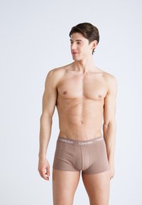 Bruine katoenen boxershorts met een logoopdruk op de tailleband. Het ontwerp heeft een strakke pasvorm en een gladde textuur, benadrukt door minimalistische kleuren.
