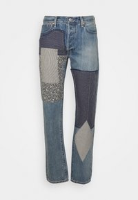 Džínové kalhoty s modrým praním a různými panely z patchworku v pruhovaném, květinovém a texturovaném materiálu, vytvářejícími vizuálně výrazný design.