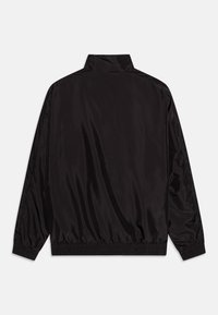 Musta kevyt takki, jossa on korkea kaulus, joustavat hihansuut ja kerrostettu helma. Soljuva, kiiltävä kangas ilman näkyvää raudustusta tai kuvioita.