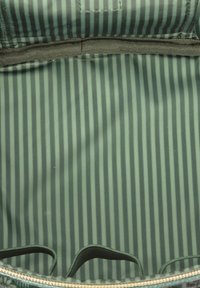 Groene stoffen binnenkant van een tas met verticale strepen, afgewerkt met zwarte bies, zachte textuur en twee stoffen handvatten voor gemakkelijk dragen.