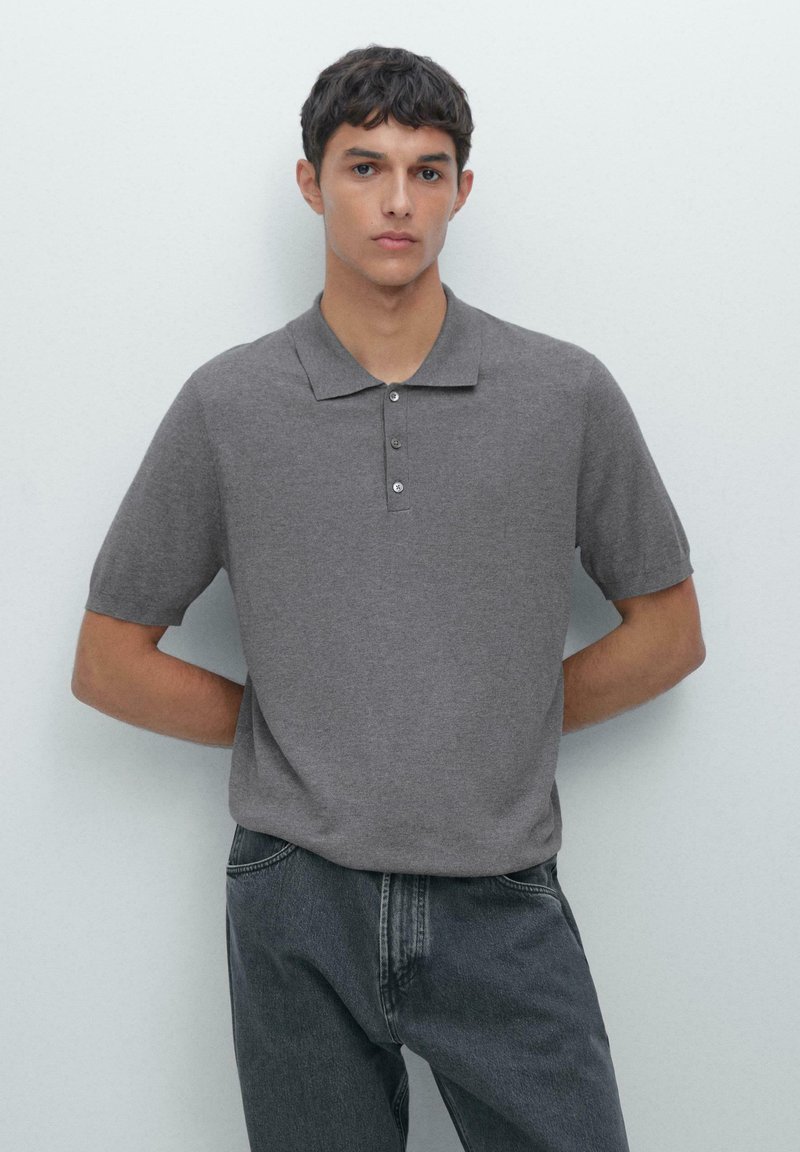 Polo grigio con colletto, maniche corte e pattina con tre bottoni, abbinato a jeans grigio scuro. Texture liscia.