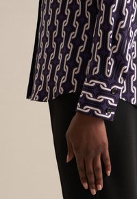 Camicia a maniche lunghe viola con un motivo a catena bianco e viola scuro, con polsini con bottoni e una trama di tessuto liscia.