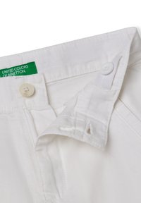 Tessuto di cotone bianco di un paio di pantaloni con un'etichetta verde che recita "United Colors of Benetton." Presenta un bottone bianco e dettagli cuciti.