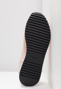 Parte inferior de caucho negro con ranuras texturizadas; parte superior en materiales rosa claro y gris, con un patrón de panal y marca.