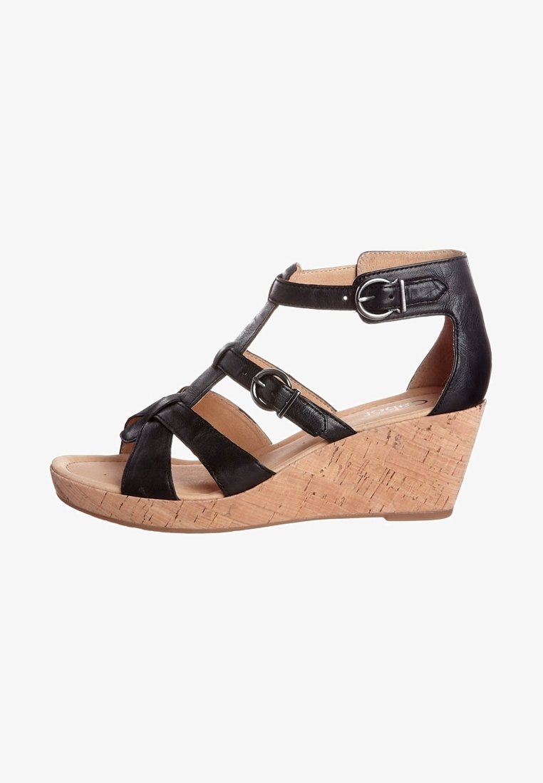 Sandalo con zeppa in pelle nera, caratterizzato da cinturini incrociati, una fibbia argentata e un tacco con texture di sughero. Design con punta aperta per una migliore traspirabilità.